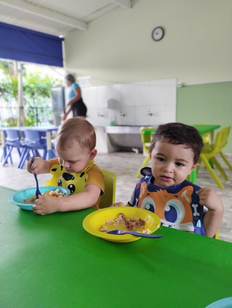 Bebês em cadeirão durante a refeição no berçário, vista ampla