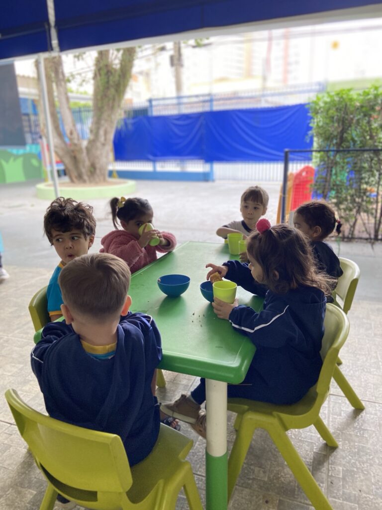 Turma reunida em mesas na área externa da escola durante a refeição