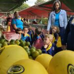 Criança segurando fruta ao lado da feirante durante passeio à feira