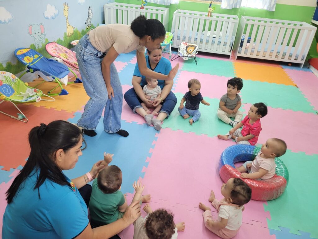 Bebês em tapete colorido com a professora na sala do berçário, outro ângulo
