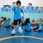 Criança se apresentando em pé diante da turma sentada na aula de musicalização